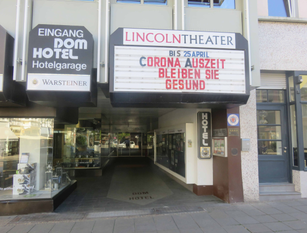 Das Lincoln Theater in Berlin, Deutschland, ein Gebäude mit Glasfenstern und -türen und einer Tafel mit Text darauf, mit verschiedenen Gegenständen im Inneren, die einen belebten Stadtbild geben.