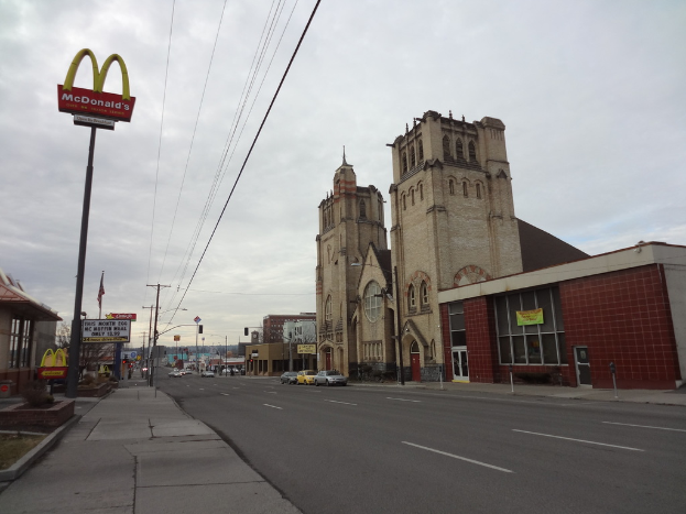 Eine Straßenansicht mit Gebäuden auf der rechten Seite, Pfählen und Autos in der Mitte und einer McDonald's-Stange auf der linken Seite.