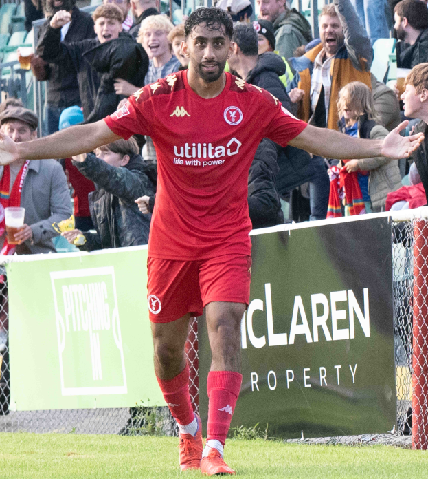 Ein Fußballer in roter Uniform rennt mit ausgebreiteten Armen auf einem Feld, mit einer Zuschauermenge im Hintergrund und einem Banner mit der Aufschrift "Middlesbrough FC vs. Swansea City - Sky Bet Championship" im Vordergrund.