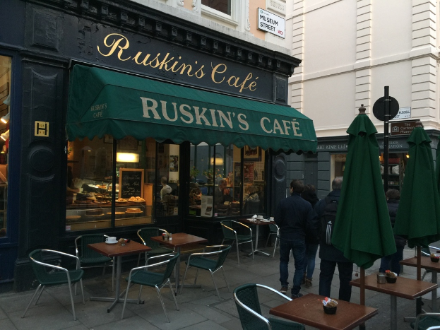 Eine Gruppe von Menschen vor einem Café mit der Aufschrift "Ruskin's Cafe".