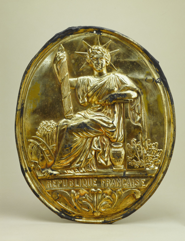 Goldene runde Plakette mit einem reliefartigen Statue of Liberty-Design und eingraviertem Text, vor einem weißen Hintergrund.