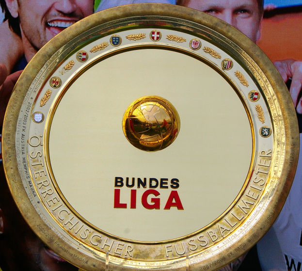 Goldener Schild mit "Bundesliga"-Text in der Hand eines Mannes, im Hintergrund eine Fahne mit drei Personen.