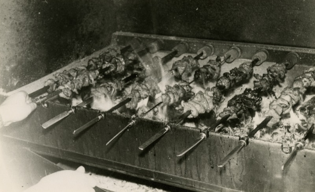 Eine Person grillt Kebabs, wobei ihre Hand auf der linken Seite des Bildes zu sehen ist.