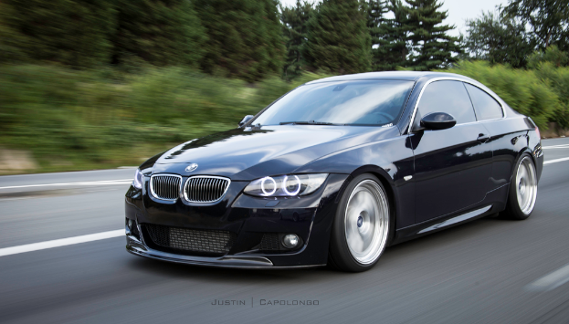 Ein schwarzer BMW auf einer Stra├če mit B├Ąumen im Hintergrund.