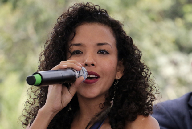 Eine Frau singt in ein Mikrofon, neben ihr steht ein Mann, vor einem unscharfen Publikum.