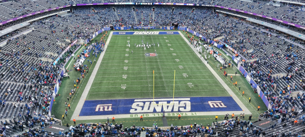Ein voller Fußballstadion mit Spielern auf dem Feld, Torpfosten und Zuschauern auf den Tribünen unter einer lebendigen Atmosphäre.