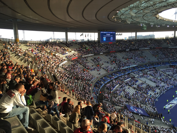 Große Menschenmenge in einem Stadion bei einem Fußballspiel mit einer Bühne, Fahnen, Stangen und einem Bildschirm im Hintergrund