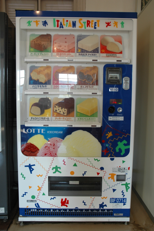 Ein Automaten mit verschiedenen Snacks, eine Münzschlitz oben, eine Ausgabe unten, eine Wand im Hintergrund und ein Fenster zur Seite.