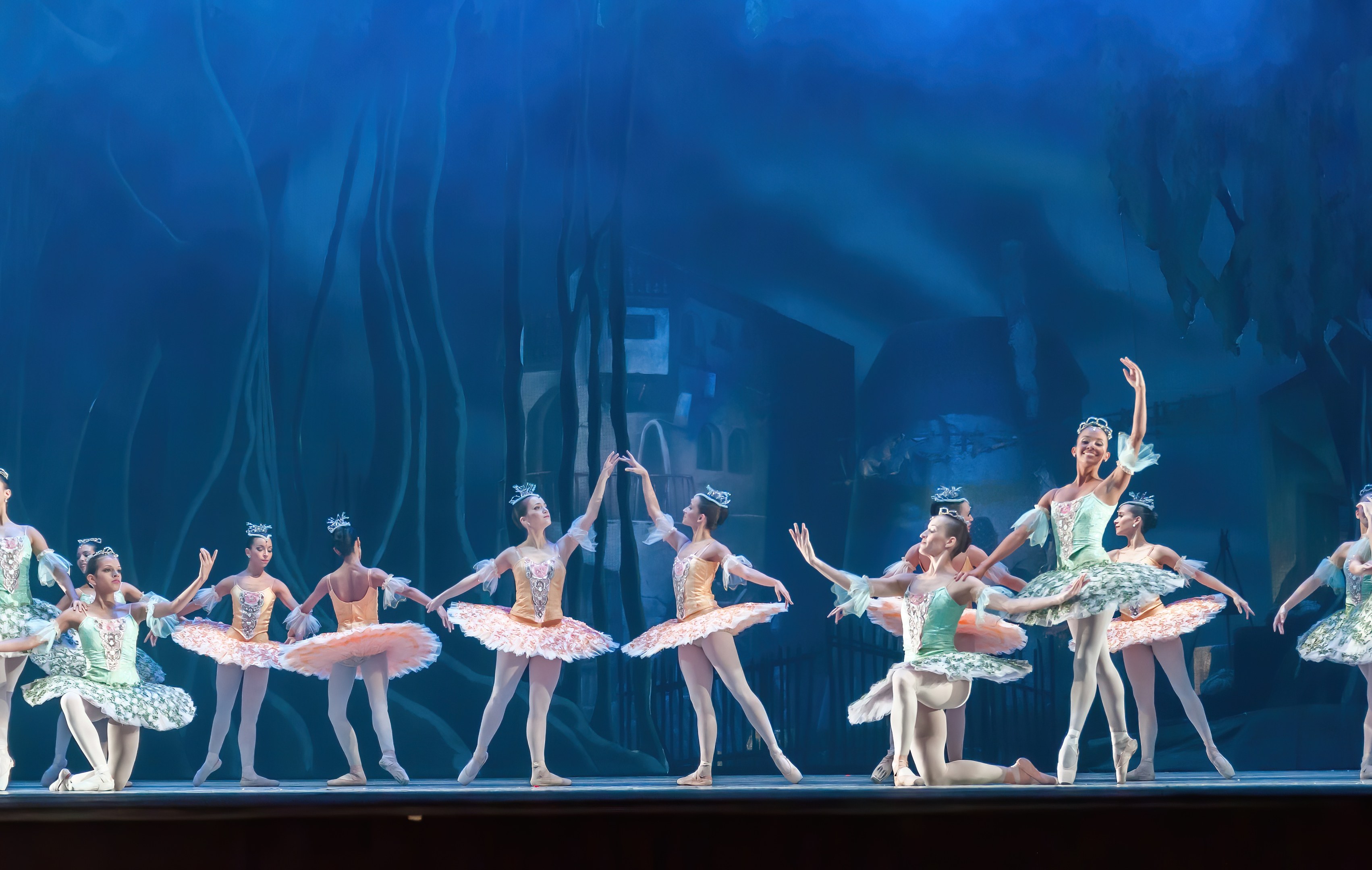 Eine Gruppe von Balletttänzern in farbenfrohen Kostümen, die *Der Nussknacker* auf der Bühne des Royal Opera House tanzen, bewegen sich synchronisiert gegen einen blauen Hintergrund.