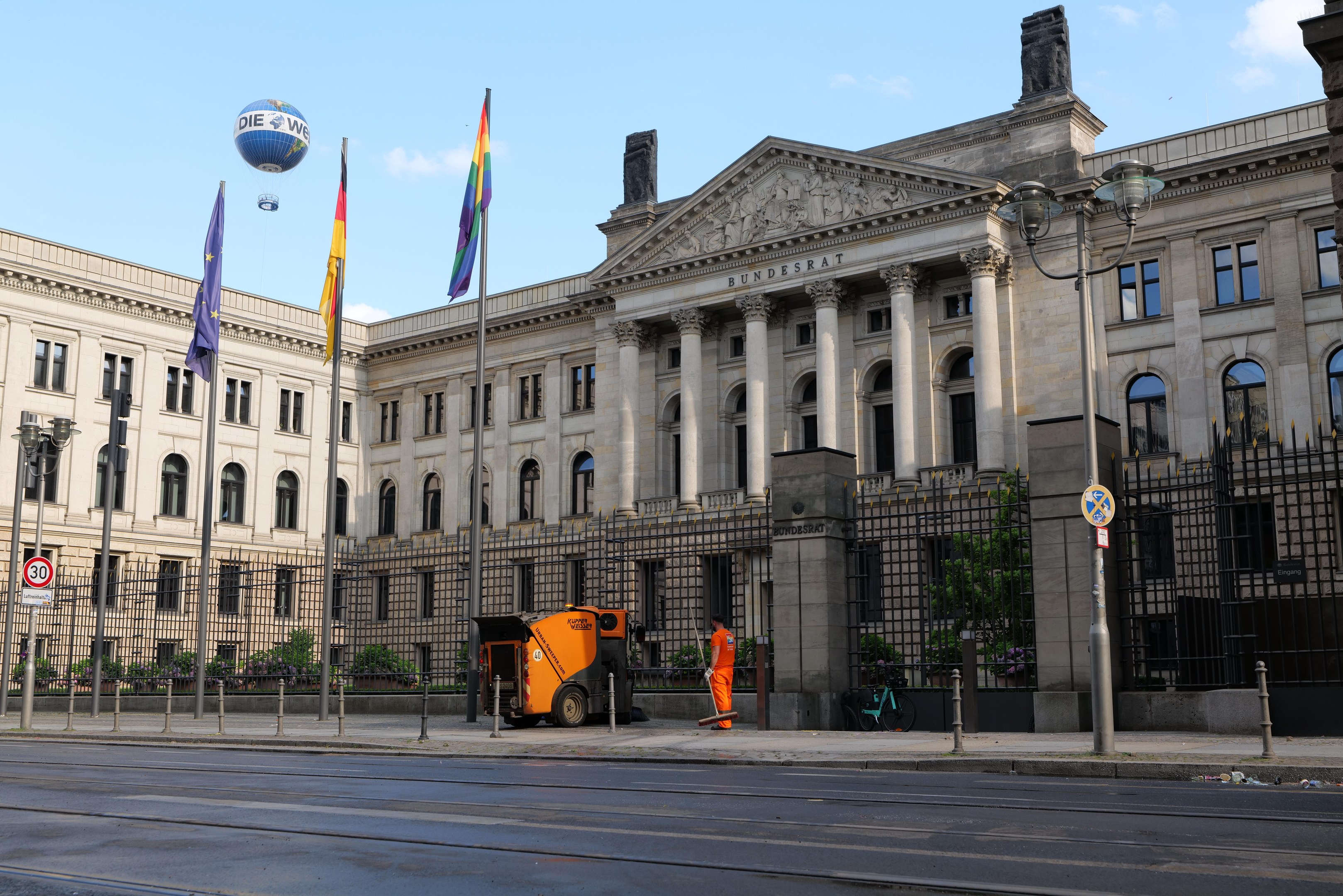 Großes modernes Regierungsgebäude (Bundestag) in Berlin mit vielen Fenstern, umgeben von Straßeninfrastruktur und Fußgängern, unter einem bewölkten Himmel.