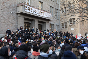 Eine große Menge von Menschen mit Masken und Schildern versammelt sich vor einem Gebäude in Warschau, Polen, um das Ende der Coronavirus-Pandemie zu feiern, mit einem Banner und einem Baum auf der rechten Seite.