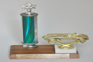 Ein glänzender, detaillierter Pokal mit einem Miniaturauto darauf, auf einer hellen Holzplatte präsentiert.