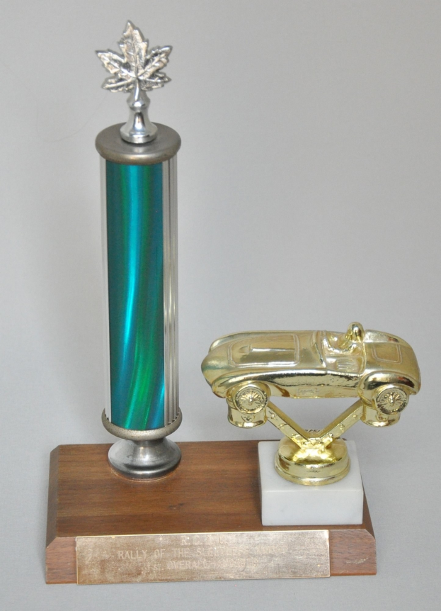 Ein glänzender, detaillierter Pokal mit einem Miniaturauto darauf, auf einer hellen Holzplatte präsentiert.