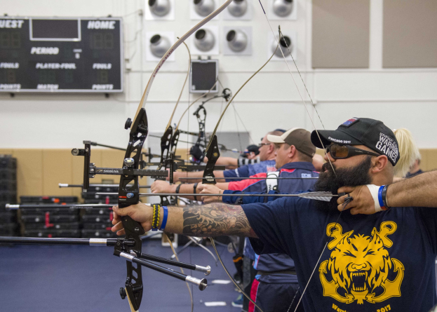 Eine Gruppe von Bogenschützen in Mützen bei der Indoor-Praxis während der World Archery Championships 2017, mit einer Texttafel links und Equipment rechts.