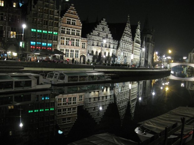 Zwei weiße Boote liegen an einem kleinen Wasserteich, dahinter sind Burggebäude und Straßenlaternen zu sehen, im Hintergrund eine alte Brücke.