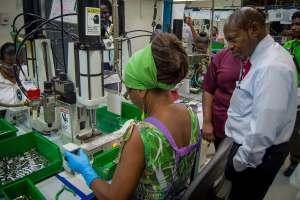 Eine Frau bedient eine Maschine mit einem Warnschild, umgeben von Kabeln, Papieren und Gegenständen in einem grünen Behälter.