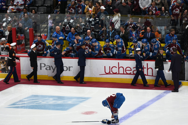 Eishockeyspieler auf dem Eis umgeben von Teamkollegen und Gegenspielern während eines Spiels, mit Zuschauern und Brettern, die "Colorado Avalanche vs San Jose Sharks - 3/24/15 NHL Pick, Odds, and Prediction" anzeigen, im Hintergrund.