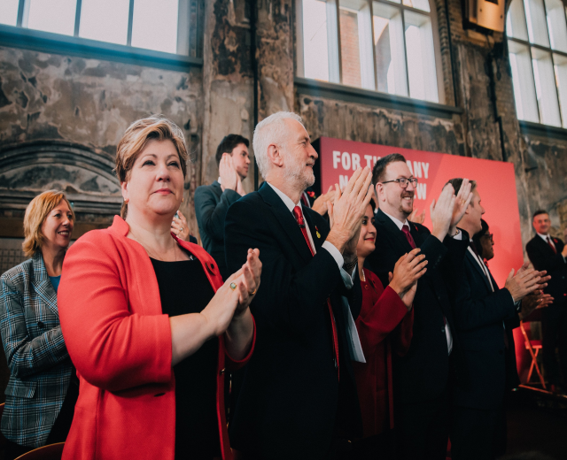 Eine Gruppe von Menschen, die vor einer Menge jubeln, mit einem Banner im Hintergrund, auf dem "Wir haben die Wahl gewonnen." steht