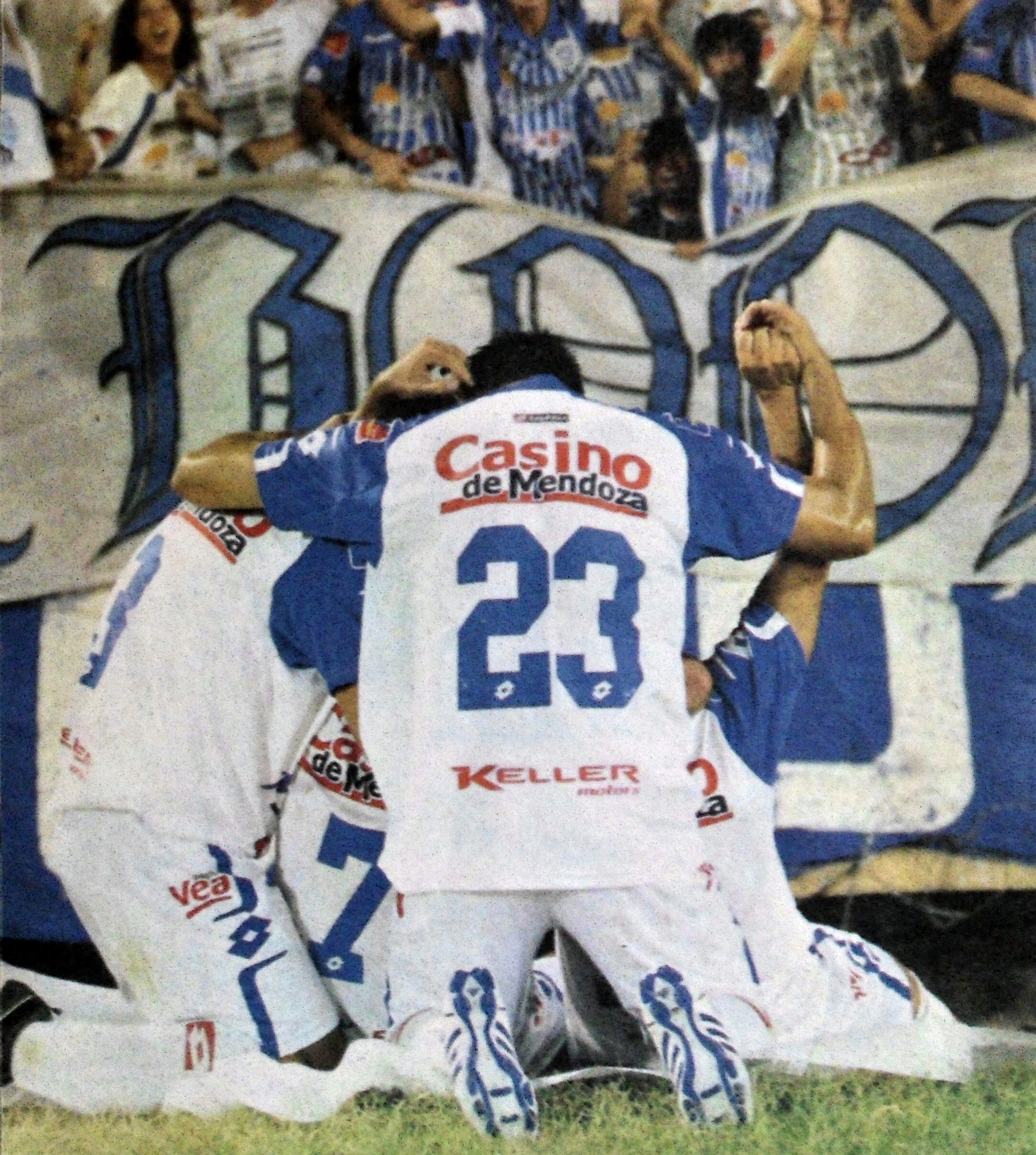 Gruppe von Fußballspielern, die auf dem Boden vor einer jubelnden Menge mit einem Banner feiern.