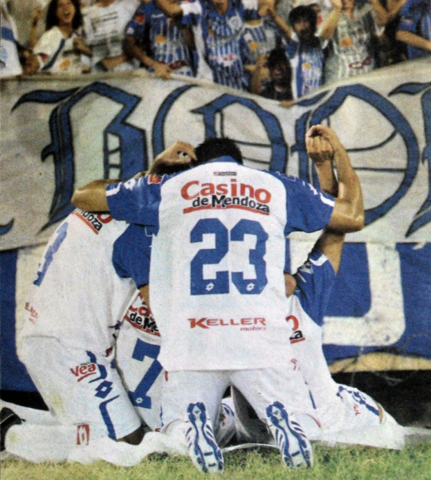 Gruppe von Fußballspielern, die auf dem Boden vor einer jubelnden Menge mit einem Banner feiern.