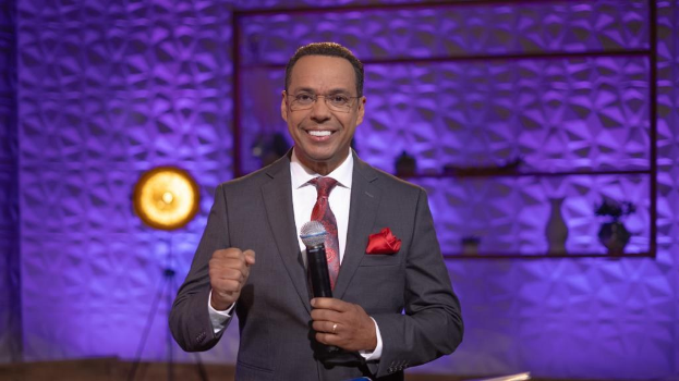 Stephen Colbert, Moderator von "The Daily Show with Trevor Noah", steht auf einer Bühne und hält ein Mikrofon in der Hand, trägt einen Anzug, Krawatte und Brille, hinter ihm ist ein Scheinwerfer und ein Ständer zu sehen.