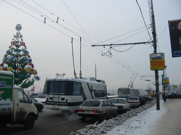 Eine belebte Stadtstraße mit Verkehr, Schnee und einem Weihnachtsbaum, mit Passanten, Gebäuden und einem klaren Himmel im Hintergrund.